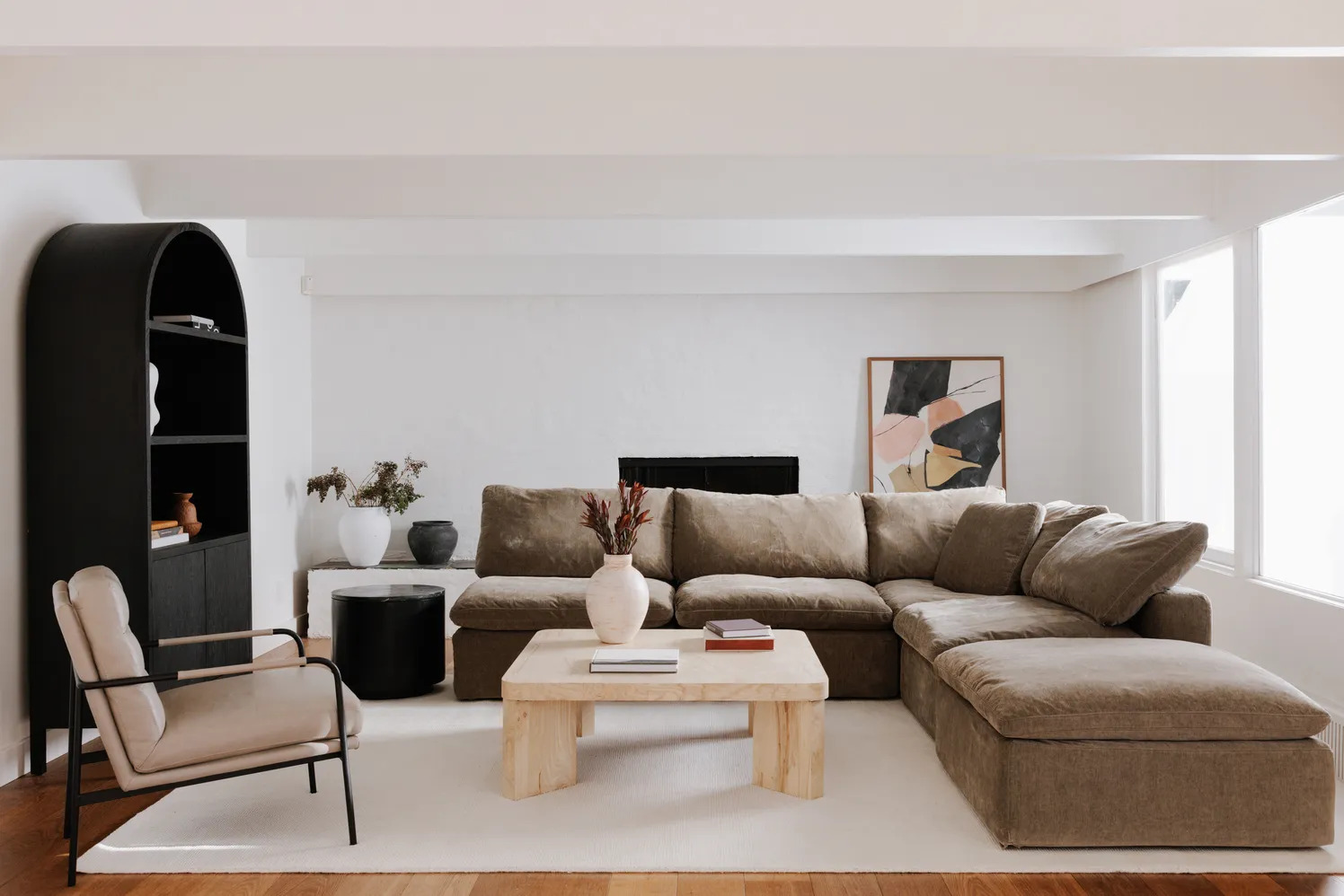 A living room with a tan sectional couch and a mid-century modern style black leather chair.
